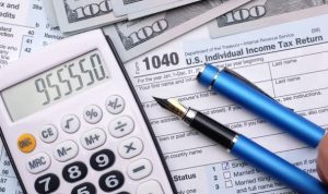 Tax form 1040, pen, dollar bills, and calculator. High angle view.